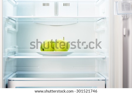 Two green apples on white plate in open empty refrigerator. Weight loss diet concept.