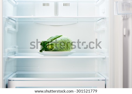 Green cabbage on white plate in open empty refrigerator. Weight loss diet concept.