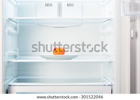 Two-colored orange and red peach on white plate in open empty refrigerator. Weight loss diet concept.