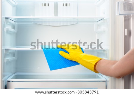 Woman\'s hand in yellow rubber protective glove cleaning white open empty refrigerator with blue rag