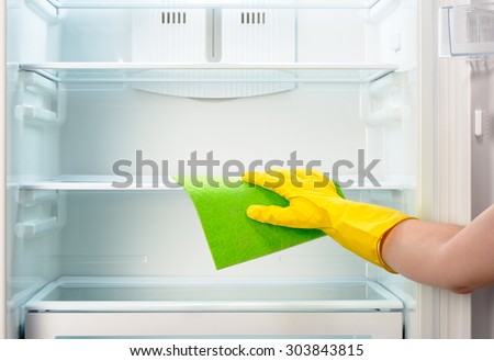 Woman\'s hand in yellow rubber protective glove cleaning white open empty refrigerator with green rag