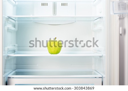 Green apple on shelf of open empty refrigerator. Weight loss diet concept.