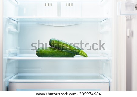 Two green zucchini on shelf of open empty refrigerator. Weight loss diet concept.