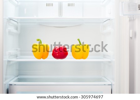 Two yellow and one red peppers on shelf of open empty refrigerator. Weight loss diet concept.