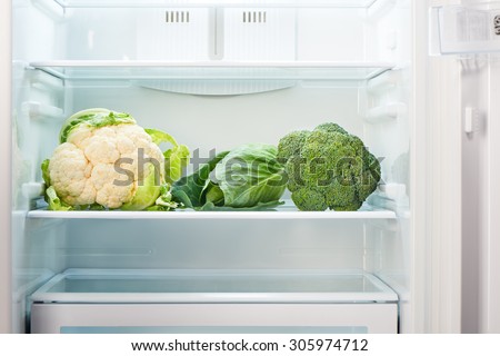 Cauliflower, green cabbage and green broccoli on shelf of open empty refrigerator. Weight loss diet concept.