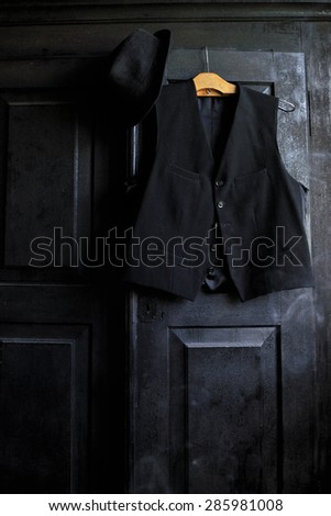 A black waistcoat on a wooden hanger and a black hat