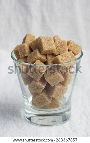 Brown sugar cubes in a transparent mug over white cloth
