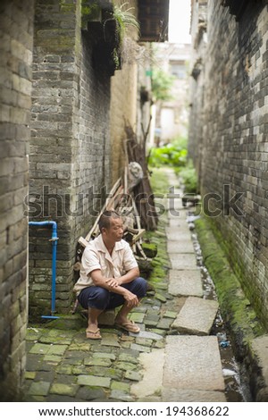 GUANGZHOU, CHINA - MAY 19: An unidentified old village man is sitting at the hallway in a very old village near Guangzhou, China on May 19 2014.