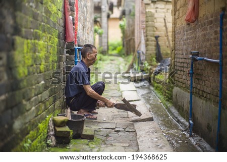 GUANGZHOU, CHINA - MAY 19: An unidentified old village man is preparing wood for cooking at the hallway in a very old village near Guangzhou, China on May 19 2014.