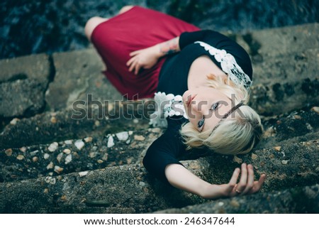 Hippy adult female laying down on stone steps looking up at camera wearing red skirt and a black shirt with a white vest