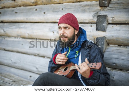 bearded guy playing guitar in mountains near wooden house