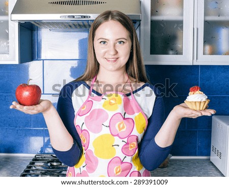 young caucasian woman trying to choose cupcake or apple on kitchen, healthy lifestyle concept