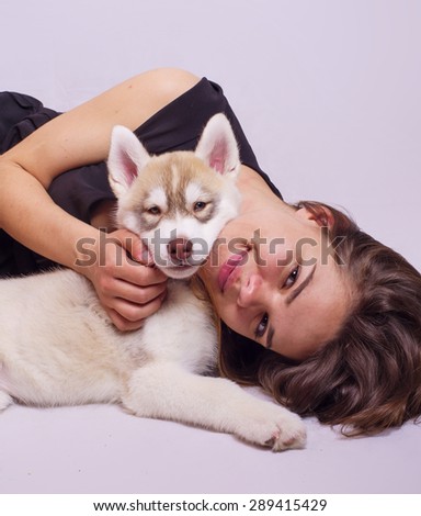 young caucasian female playing with a puppy, girl and siberian husky studio shot on grey background