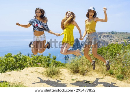 three young cheering  friends jumping on a cliff above the sea