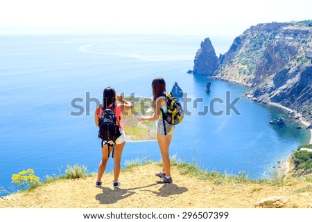 young caucasian females with backpacks and map on a cliff above the sea, hikers looking at map and try to find a way