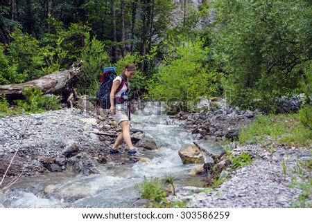 Caucasian hiker woman crossing the river on trek in mountains with backpack living a healthy active lifestyle. Hiker girl on nature landscape hike in Crimea.