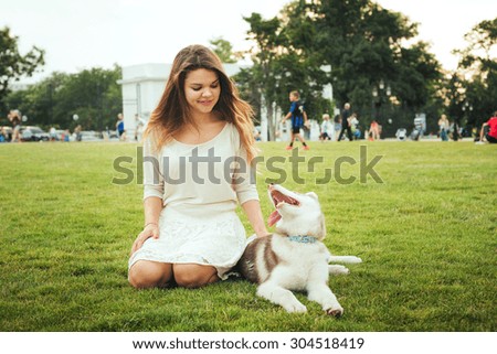 young caucasian female sitting on green grass with siberian husky puppy in the park
