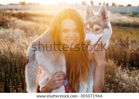 young caucasian female playing with her siberian husky puppy in the field during the sunset. Happy smiling girl having fun with puppy outdoors in beautiful light