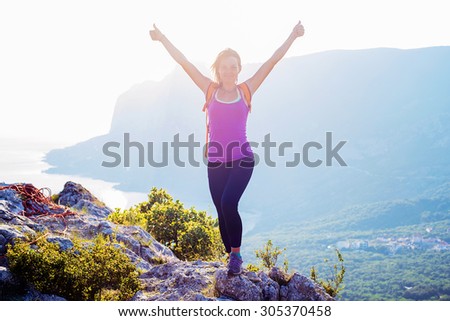 free happy caucasian female standing on the top of mountain with cheering hands. active and healthy woman hiking in mountains in crimea