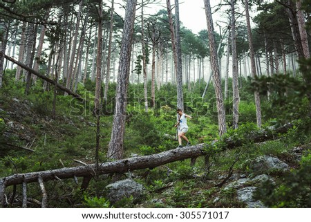 Caucasian hiker woman on trek in mountains living a healthy active lifestyle. Hiker girl on nature landscape hike in Crimea balancing on a tree, happy free female in the wood.