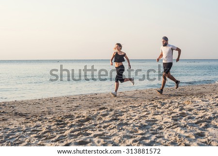 Running people - woman and man athlete runners jogging on beach. Fit young fitness couple exercising healthy lifestyle outdoors during sunrise or sunset