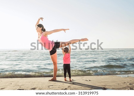family workout - mother and daughter doing exercises on beach. Mom and child working out on seaside in the morning. Healthy lifestyle concept