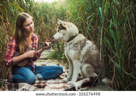 young caucasian woman playing ukulele. Female with siberian husky dog playing guitar outdoors