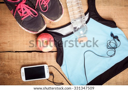 Sport equipment. Sneakers, water, apple, blue top, smartphone and earphones on wooden background. Clothes for running