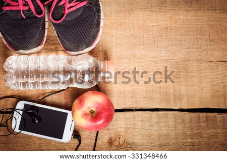 Sport equipment. Sneakers, water, apple, smartphone and earphones on wooden background. Clothes for running. Morning running concept