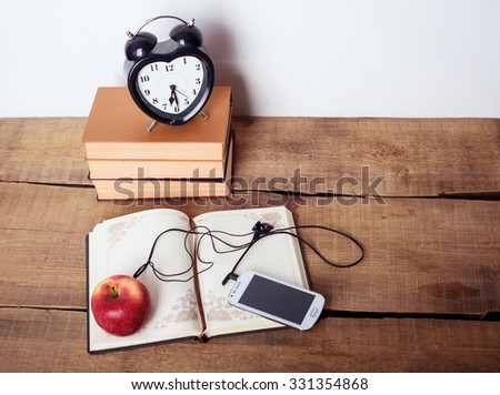 books, alarm clock, notepad, cellphone with earphones and apple on wooden background. Education equipment, education concept
