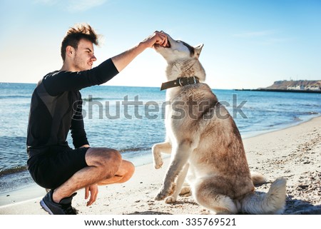sporty male playing with two husky dogs on beach