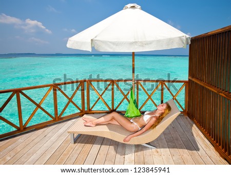 Young woman tans on a water villa terrace , Maldives