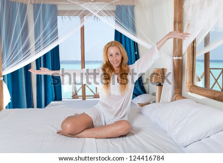Young pretty woman in bed with sea behind window.