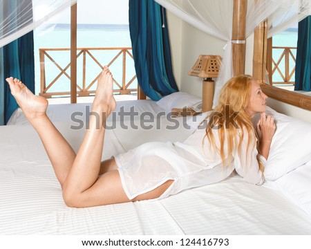 Young pretty woman in bed with sea behind window.