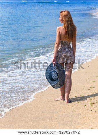 Young beautiful woman goes on ocean coast with straw hat in hands