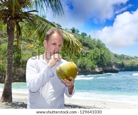 attractive man drinks coconut juice from a nut on a beach at the sea