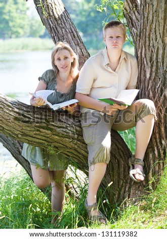 Young guy and the girl prepare for lessons, examination in spring park near lake