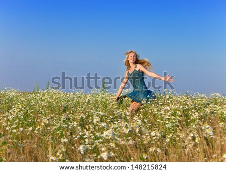The happy young woman jumps in the field  of chamomiles