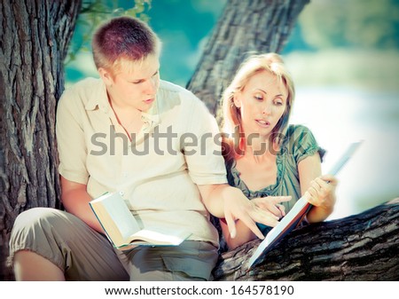 Young guy and girl with books on the nature near lake,with a retro effect