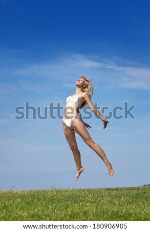 The happy woman jumps in a summer green field against the blue sky