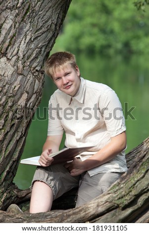 The young man with the book in park on the bank of lake