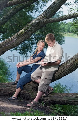 Young guy and the girl prepare for lessons, examination in spring park near lake