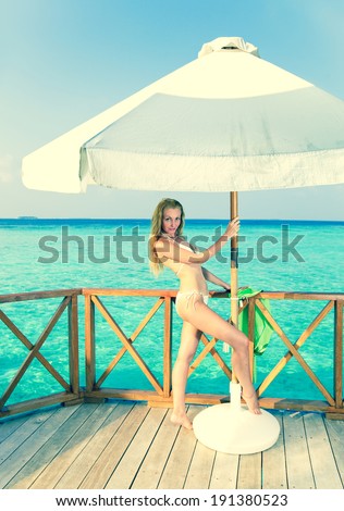 Young woman tans on a water villa terrace , Maldives,with a retro effect