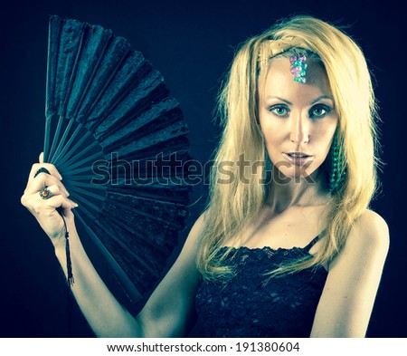 The beautiful young woman with long  blonde hair and  fan on  dark background,with a retro effect
