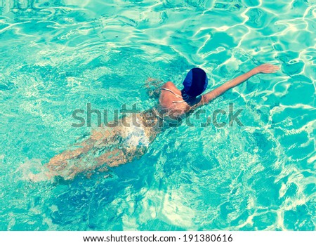 The sporting woman swims in bright blue water,with a retro effect