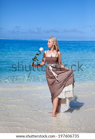 The young beautiful woman in a romantic dress with a rose on sand at the sea edge