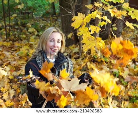The beautiful woman in autumn park throws up maple leaves