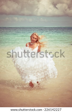 The young beautiful woman in a dress of the bride runs on waves of the sea,with a retro effect