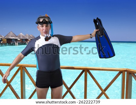 Young sports man with flippers, mask and tube on sundeck of a house over the sea. Maldives