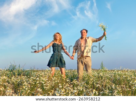 Happy man and the woman jump in the field with camomiles